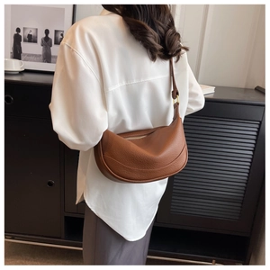 Detail view of a brown pebbled leather crescent shoulder bag worn by a model