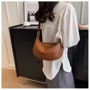 Brown lychee leather crescent shoulder bag worn with casual outfit in lifestyle setting