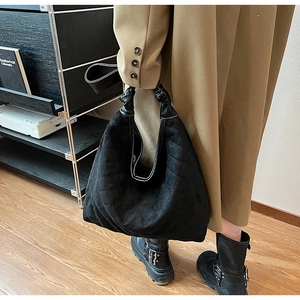 Detail of black quilted dumpling bag featuring a unique knotted handle and suede texture