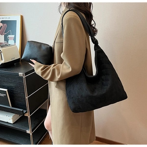 Close-up of quilted black suede tote bag with knotted strap and matching cosmetic pouch