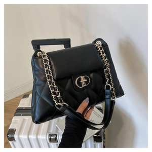 Close-up of black quilted leather shoulder bag with a gold circular metal lock and chain