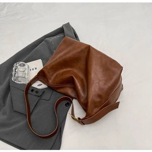 Detail van bruine leren tas met verstelbare schouderband op een grijze blazer jas