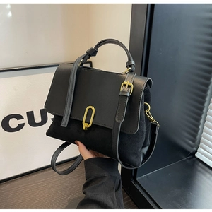 Detail of black leather handbag featuring gold oval clasp and textured panel contrast