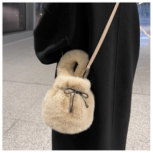 Detail view of beige faux fur bucket bag with drawstring bow and thin leather shoulder strap