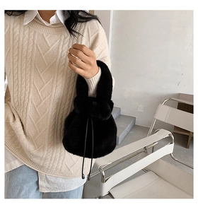 Detail of soft black faux fur bucket bag with drawstring closure held by a model