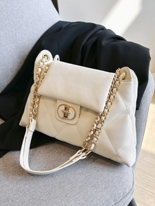 Elegant cream quilted chain shoulder bag with gold twist lock on grey fabric backdrop