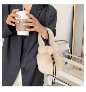 Detail of creamy white plush bucket bag with drawstring closure held by a model