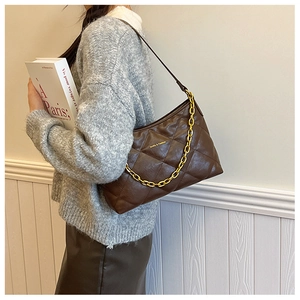 Quilted dark brown leather crossbody bag with gold chain strap on a stylish model