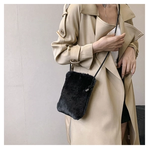 Detail of soft black faux fur crossbody phone bag with slender shoulder strap on beige coat