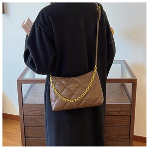 Detail view of brown quilted leather shoulder bag with gold chain on model in room