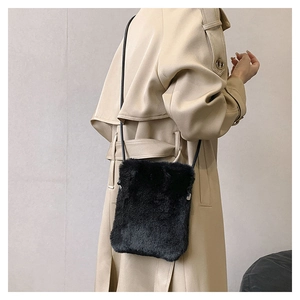 Detail of a black plush crossbody bag paired with a beige coat in a minimalist style