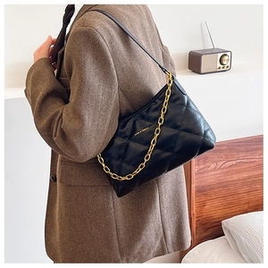 Close-up of black quilted shoulder bag with chunky gold chain and brand logo detail