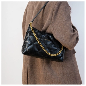 Detail of black quilted shoulder bag with chunky gold chain on herringbone blazer