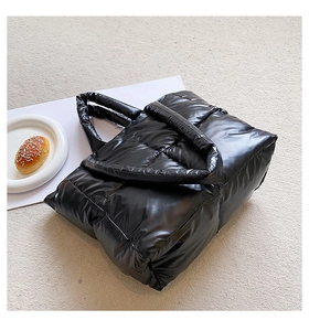Detailed close-up of a black quilted puffer tote bag with glossy finish and thick handles