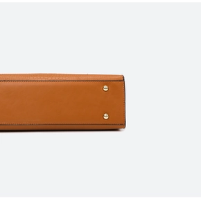 Close-up of brown embossed leather handbag with golden protective bottom metal studs