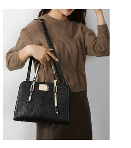 Detail of black faux snake texture tote bag with light contrasting handle and metal hardware