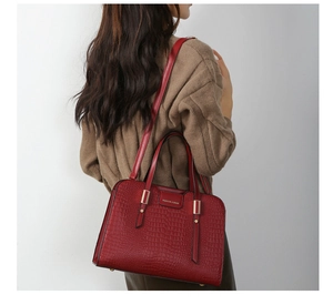 Detail view of deep red embossed crocodile pattern handbag with gold hardware