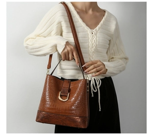Detail of crocodile embossed leather bucket bag with gold metal buckle on model