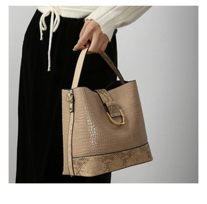 Detail of beige bucket bag with crocodile and snake skin textures and gold metal buckle