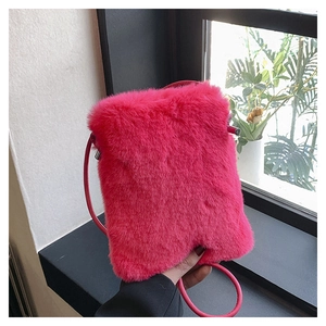 Detail view of fuchsia faux fur crossbody bag held by hand in natural window light