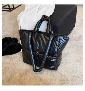 Detail of black quilted puffer tote bag with glossy nylon texture and dual straps
