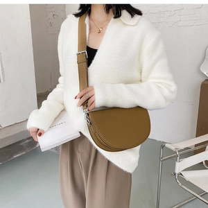Gros plan sur un sac besace en cuir caramel avec large bandoulière porté par un mannequin