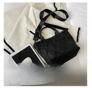 Confronto dimensioni borsa trapuntata con tablet e telefono su biancheria da letto bianca