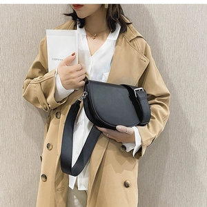 Sacoche selle noire à bandoulière large portée avec un trench-coat classique beige