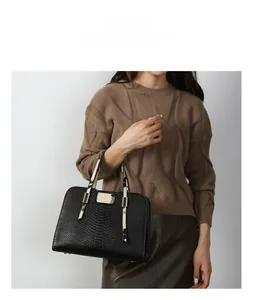 Detailed view of black snakeskin embossed handbag with contrast handles on model