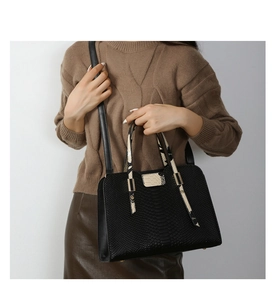 Detail of black embossed leather handbag with snake pattern trim and metal bottom studs