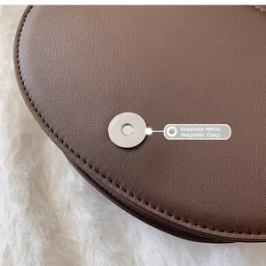 Gros plan sur la boucle magnétique en argent et les coutures de la besace en cuir marron