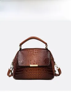 Detail view of dark brown crocodile pattern handbag with gold metal clasp and top handle