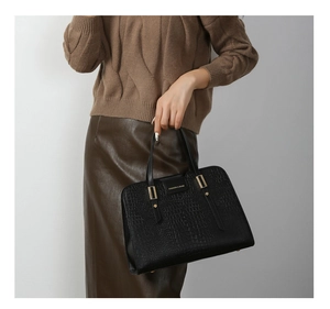Close-up of black crocodile pattern leather handbag with gold hardware and brand tag