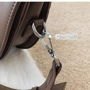 Détail macro du crochet métallique argenté sur le sac en cuir texturé marron foncé