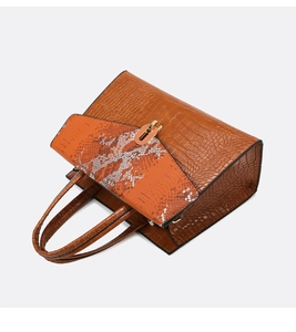 Dettaglio di una borsa in pelle di coccodrillo marrone con patta arancione e chiusura oro