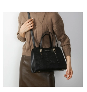 Close-up of black crocodile-embossed leather handbag with metallic logo and dual handles