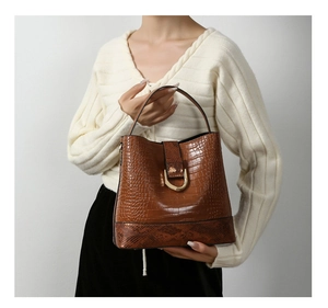 Detail of brown crocodile pattern bucket bag with golden horseshoe buckle and snake print base