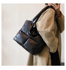 Detailed side view of a large black quilted tote bag worn with a stylish trench coat
