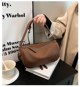Detail shot of brown pleated leather cylinder bag with silver zipper on white books