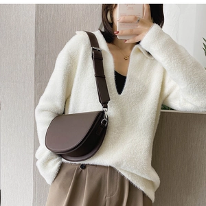 Détail d'un sac besace marron foncé avec large bandoulière porté sur un pull blanc