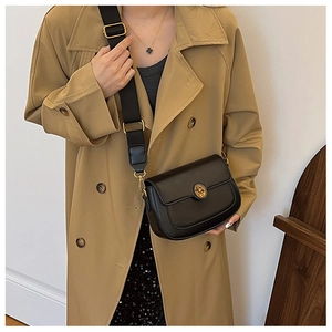 Detailed side view of a black saddle crossbody bag with golden buckle on a beige coat