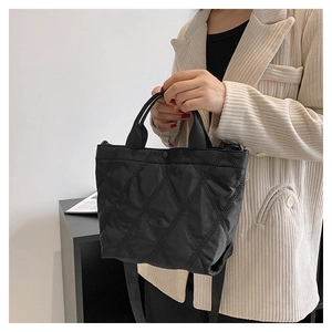 Dettaglio di una borsa tote trapuntata nera con tracolla larga indossata da una modella