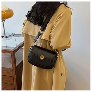 Detail of a vintage black leather crossbody bag with a gold emblem and wide shoulder strap