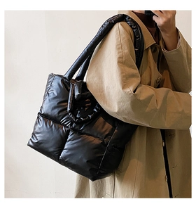 Close-up of a glossy black quilted tote bag showing padded fabric and wide shoulder strap