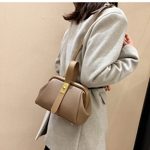 Close-up of khaki pebbled leather bag with gold metal clasp on a textured background