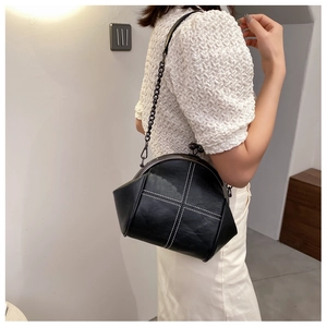 Macro detail of black retro frame bag with white cross-stitch and metal chain strap