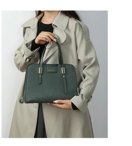 Detail of dark green embossed crocodile texture handbag worn with a grey coat