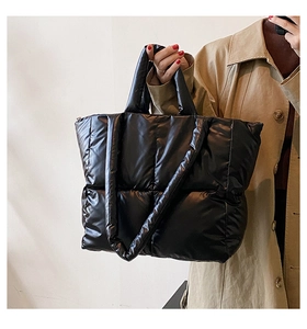 Detail of a black quilted puffer tote bag with glossy nylon finish and shoulder strap