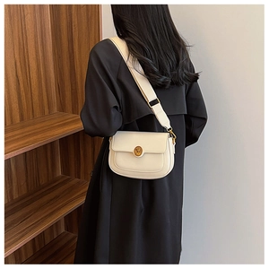 Detail of cream leather saddle bag with gold buckle on model in black trench coat