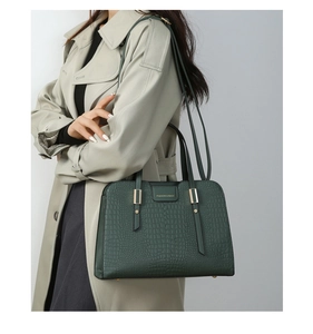 Detail of dark green embossed leather handbag with gold hardware and logo on beige coat